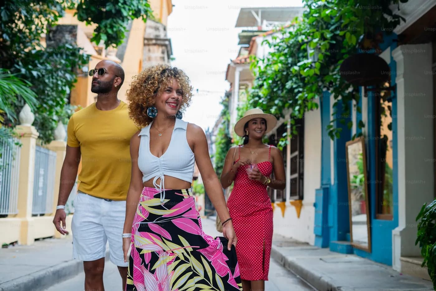 Três amigas caminhando por uma rua colonial colorida em um dia de sol